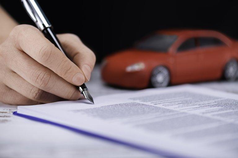 Osoba podpisuje dokument obok małego modelu samochodu osobowego